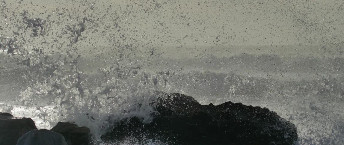 A powerful wave crashes against the rocks and water flies high into the air