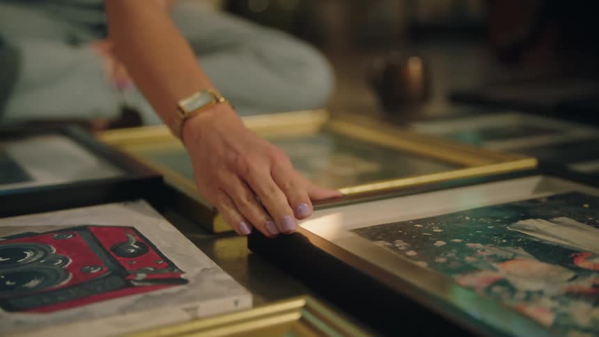 A woman is sitting on the floor arranging framed photos in front of her