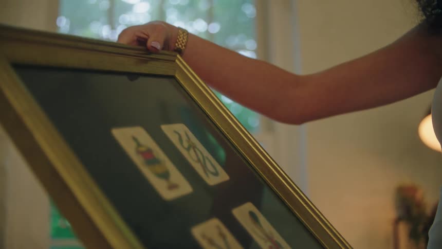 A woman whose face is not shown lifts a large picture in a frame and looks at it