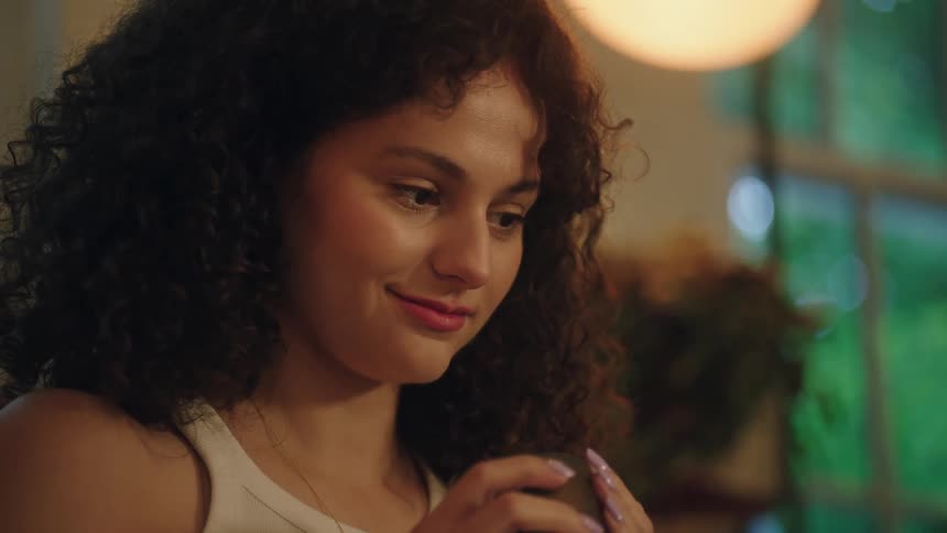 A young woman tasting a beverage indoors and then gently smiling
