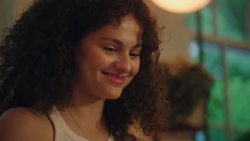 A young woman with curly hair smiles after drinking her beverage