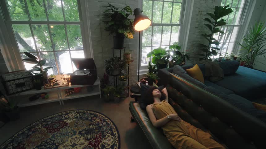 A young woman lays back onto a couch and looks up the ceiling