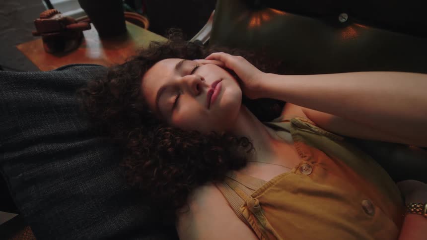 A young woman touches her face as she reclines on a couch while resting