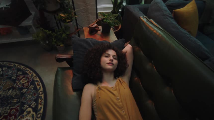 A woman lies down on a sofa and looks up at the ceiling while lost in thought