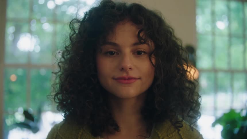 Face of a young woman with curly hair wearing a subtle smile