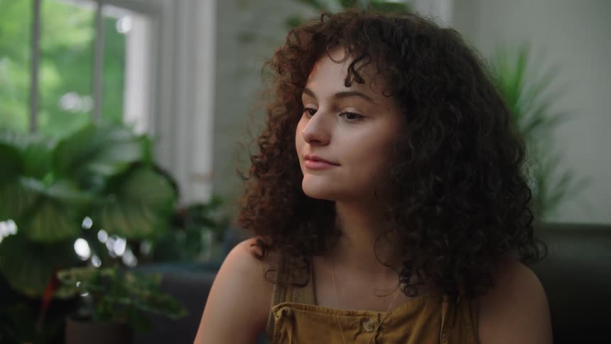 A woman with brown curly hair sitting on a couch in a living room