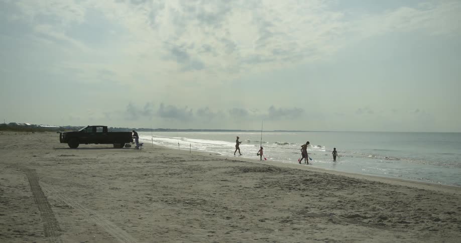 Children playing in the calm waters of the sea at a beach with a car parked on the sand