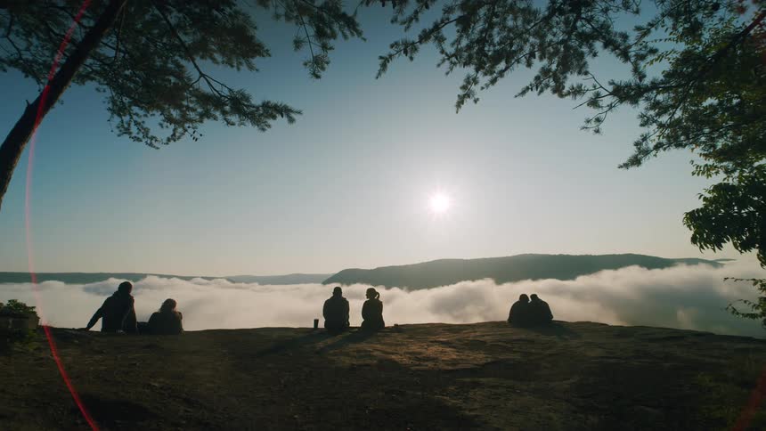 Silhouette of a group of people sitting down at the peak of a mountain