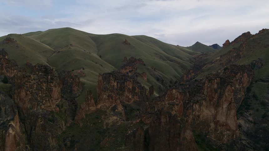 Jagged rock spires jut out from in front of high rolling hills in the distance
