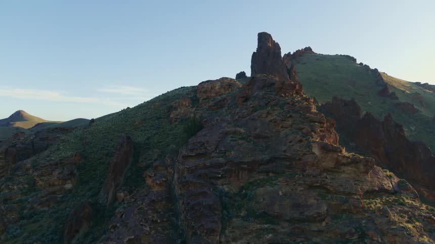 Rock formations stand on mountains as the sun shines brightly on the horizon under a clear blue sky