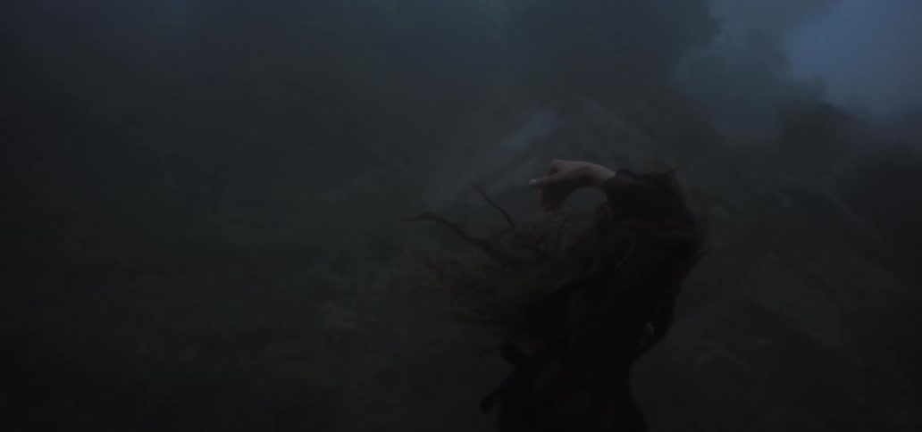 A woman dances in a dark and misty woodland during the day