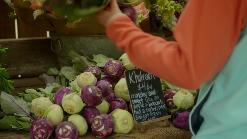 A person picks up some vegetables from a shelf on a wooden stand