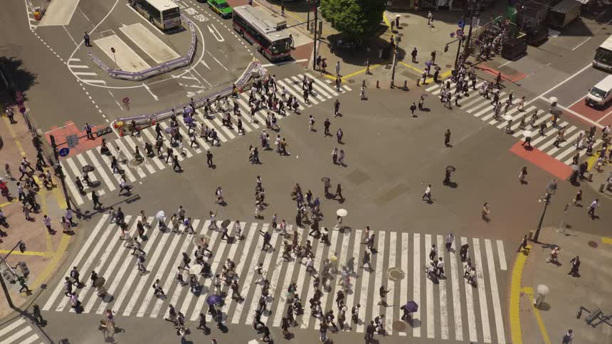 A large metropolitan crowd crossing a busy intersection of a Japanese city during the day