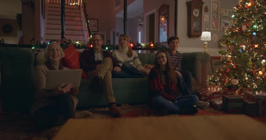 A family are sitting on the couch talking by the christmas tree