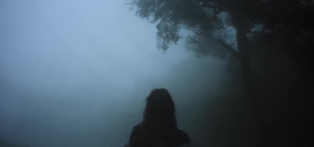 Woman with a somber look walking on a foggy forest