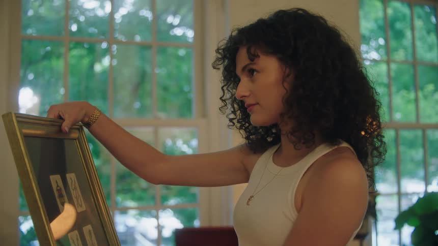 A young woman holds a framed picture and decides where to hang it in a house