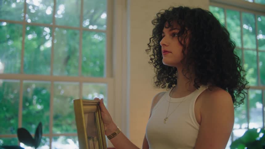 A young woman with curly hair holds a framed picture in her hands