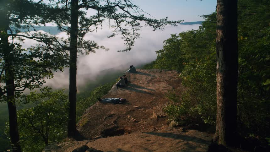 A group of people rest and recline upon a cliff overlooking a scenic valley