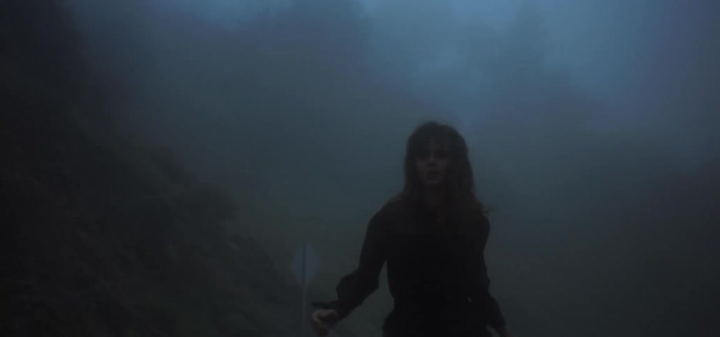 A woman in a dress runs on a road in the mountains on a cloudy day