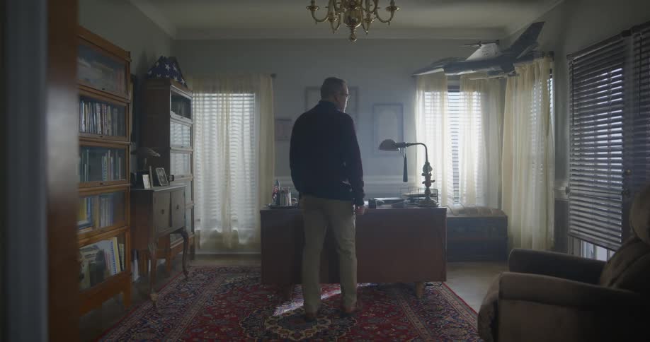 A man walks into a home office and looks at items on a desk