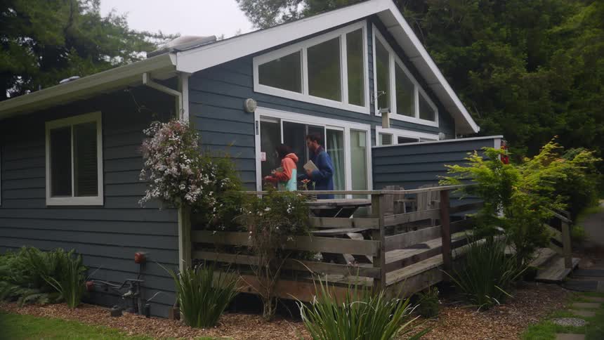 A man and woman walk from a backyard into a house with books in their hands