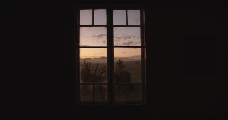 An arid landscape is visible through the window of a darkened building