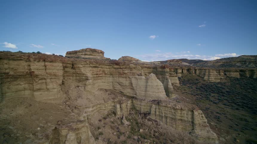 Striations of color are visable along a large mesa in the badlands under a clear blue sky