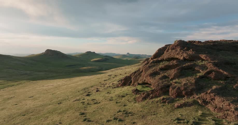 Rocks and rock formations are scattered along a shallow green valley under a painted sky