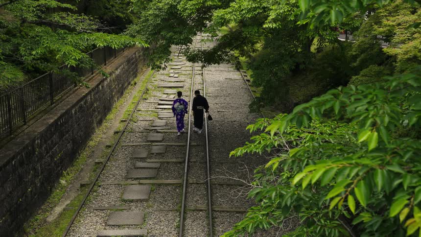 Two people wearing kimonos slowly walk around a train track in Japan