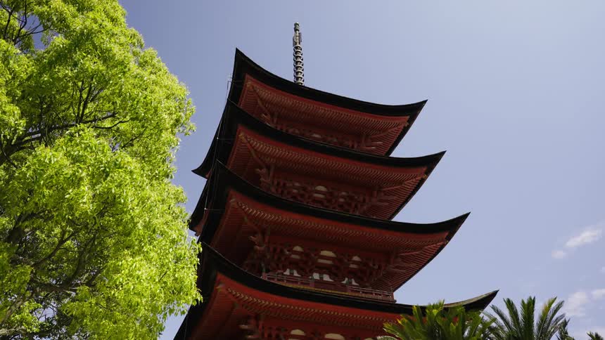 A red Japanese temple with four layers stands outside next to a tree
