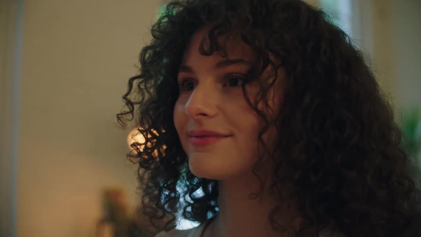 A young woman with curly hair smiles while looking at her decor