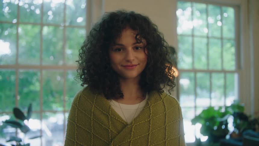A young woman with curly hair poses for the camera while indoors