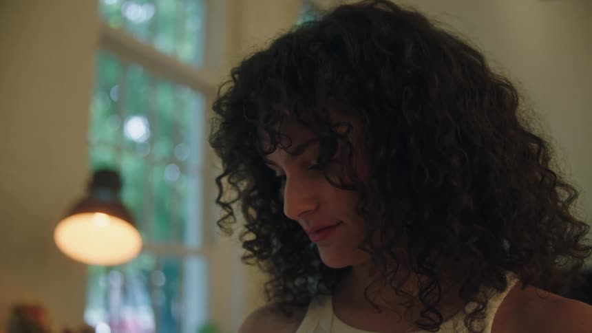 A young woman with curly hair looks down at something shes planning to place on the wall