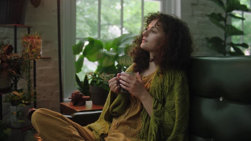 A young woman holds a beverage while relaxing on her couch