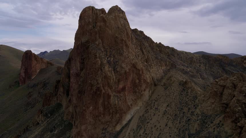 Orbit around a large spire of ancient red rock jutting out from steep terrain