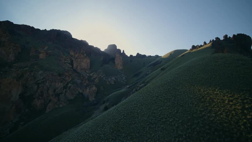 The sun peeks out from behind a jagged ridgeline in a beautiful canyon