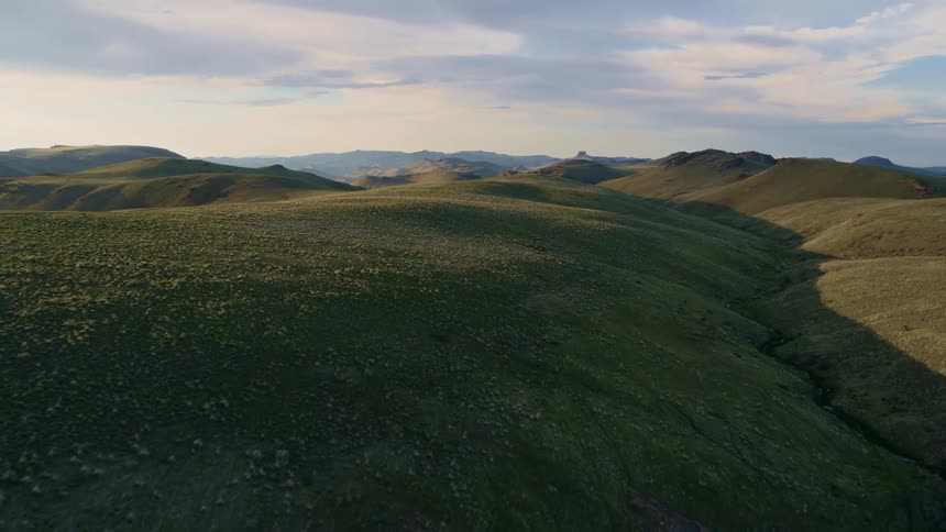 A small stream winds through sun kissed rolling green hills as far as the eye can see