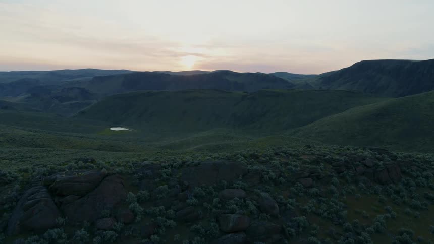Reveal of a verdant green valley as the sun hangs just above a distant mountain ridge