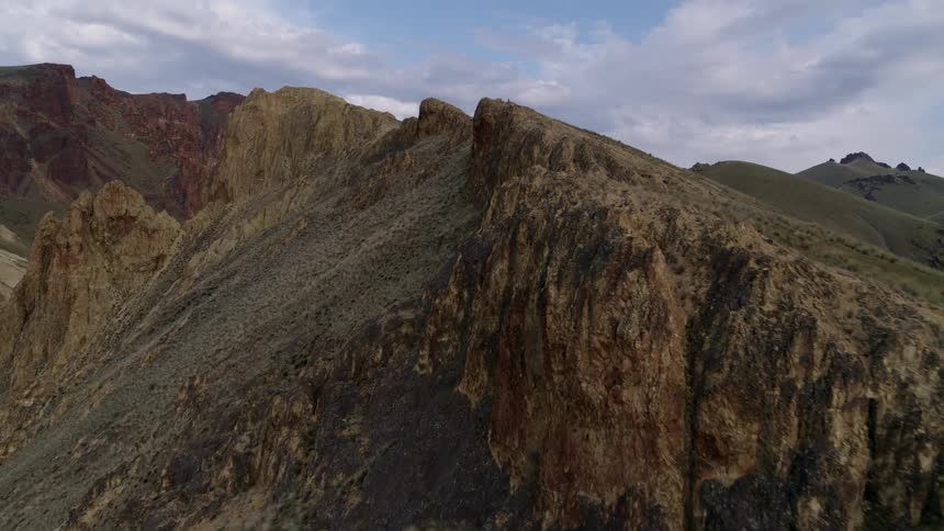 Skimming along the edge of a mountain ridge with other rock formations and sheer cliffs in the distance