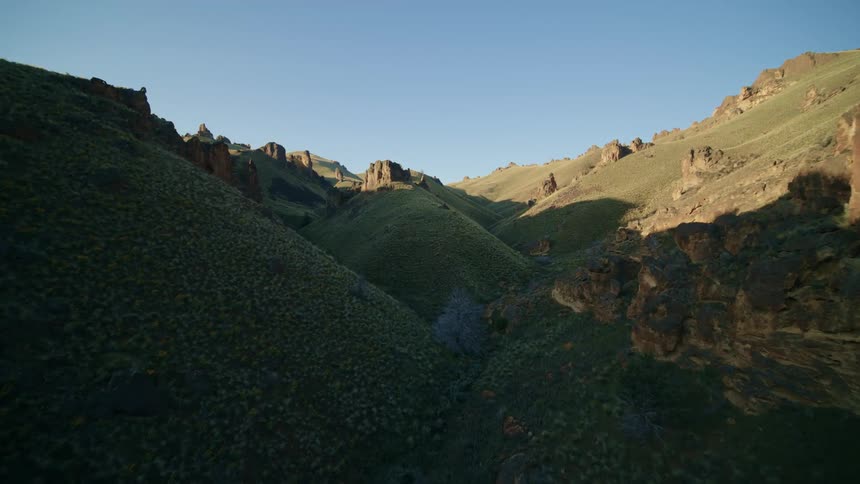 Low reveal of a magical green valley with rolling hills and rock outcroppings that climb to the sky