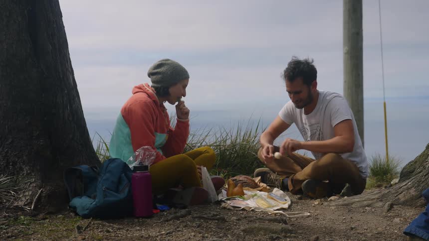 A couple eats together under a tree outdoors during the day