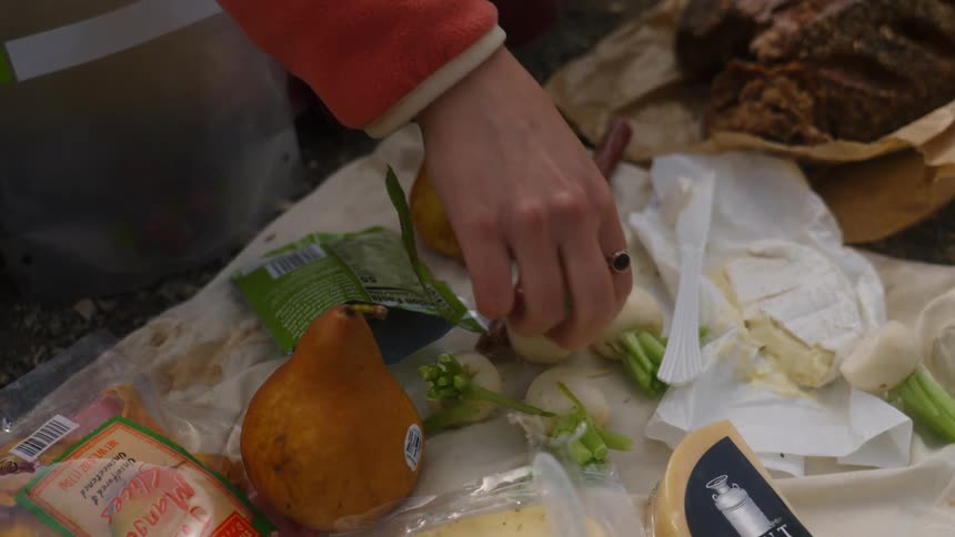 Female hand picking up a turnip from a table outdoors with many types of food