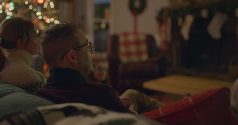 A mother and father sit on a couch while watching television together