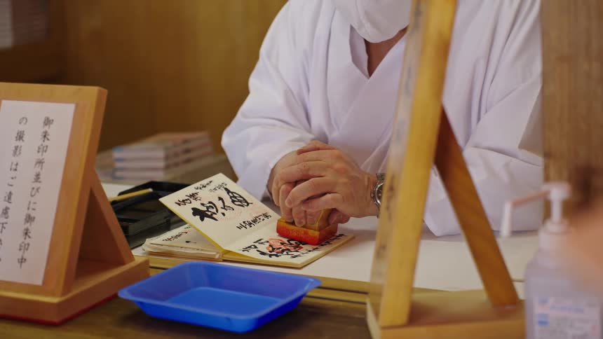 Man sitting at table with signs and hand sanitizer stamps red ink onto kanji characters in folded book