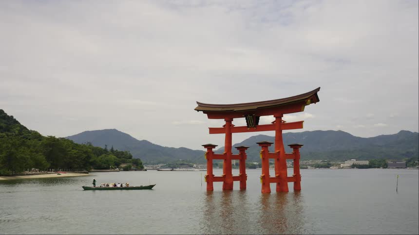 A person stands on a boat in the water near a Japanese landmark