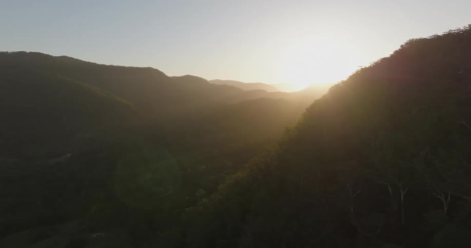 Sun shines from horizon into foggy valley between forest covered mountains
