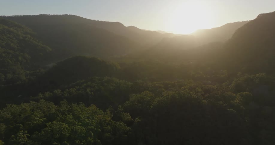 The sun shines brightly above a valley filled with dense forests