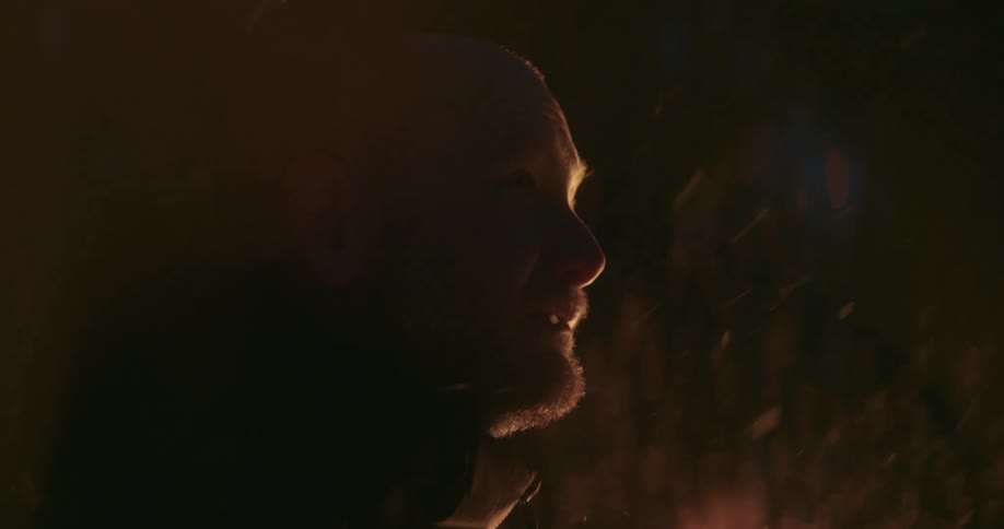 A mans face is illuminated by a nearby fire as hes outside at night