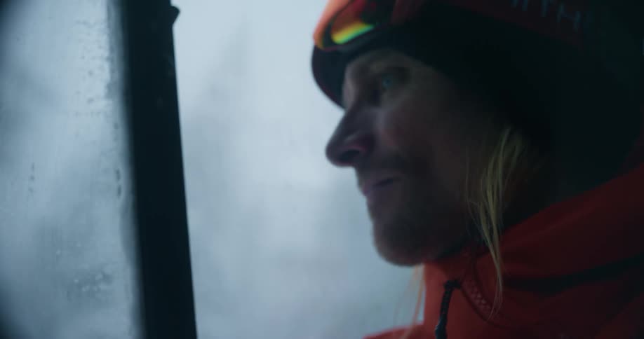 A man wearing cold weather apparel looks out a window while operating a snow plow