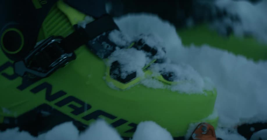 A person standing in snow tightens the straps on their plastic snow boots